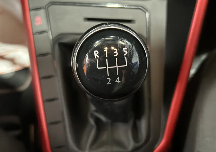Gros plan sur le levier de vitesses manuel noir de la Volkswagen Polo gris, entouré d’un cadre intérieur rouge.