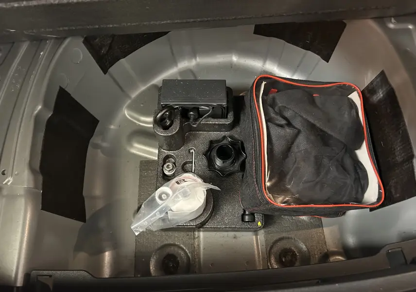 Coffre ouvert d'une Volkswagen Polo gris, vue plongeante sur le rangement sous plancher avec trousse et accessoires.