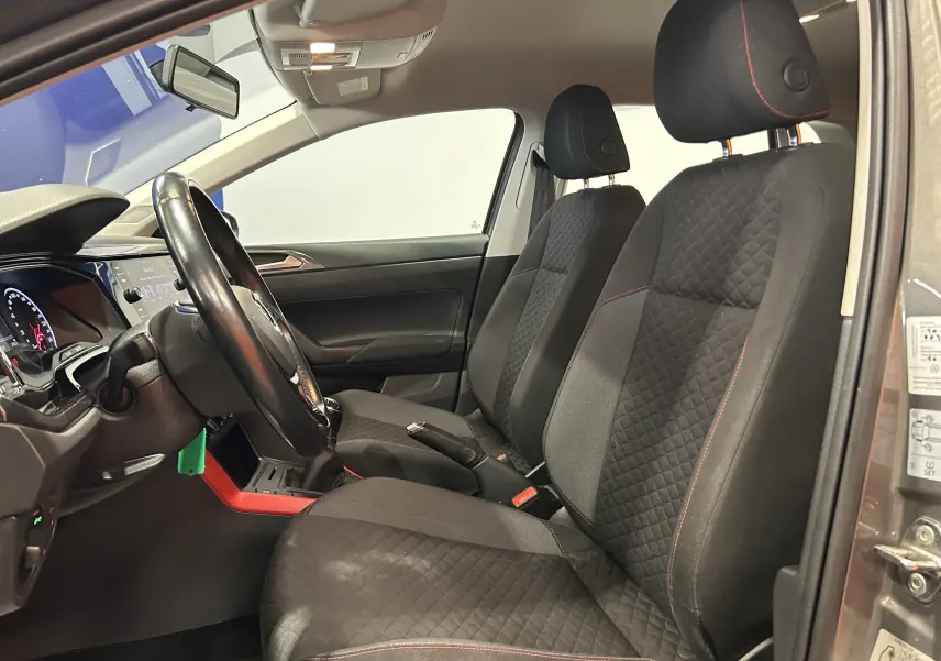 Vue intérieure côté conducteur de la Volkswagen Polo gris, sièges tissu noir avec surpiqûres rouges et volant cuir.
