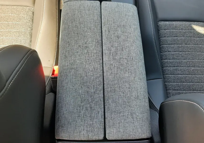 Vue plongeante sur l'accoudoir central gris tissu entre sièges avant noir et beige du Peugeot 5008 Hybrid 2025.
