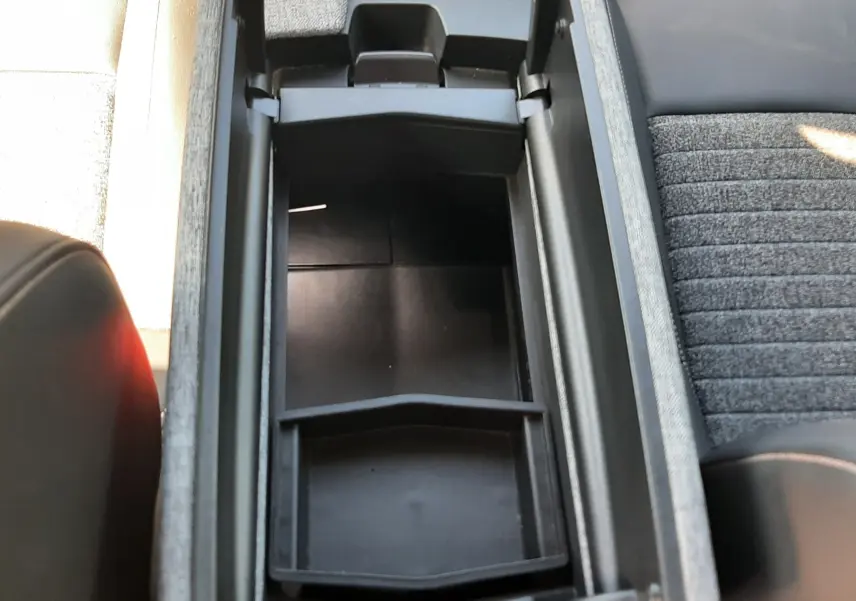 Vue plongeante sur le rangement central ouvert du Peugeot 5008 Hybrid 2025, avec console noire et sièges tissu gris.