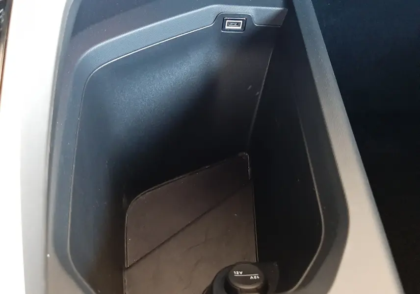 Gros plan sur le rangement central intérieur noir du Peugeot 5008 Hybrid 2025 avec prise USB et prise 12V visible.