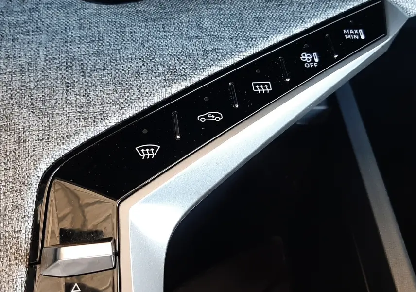 Détail de la console centrale du Peugeot 5008 Hybrid 2025 avec commandes tactiles de climatisation sur fond tissu gris.