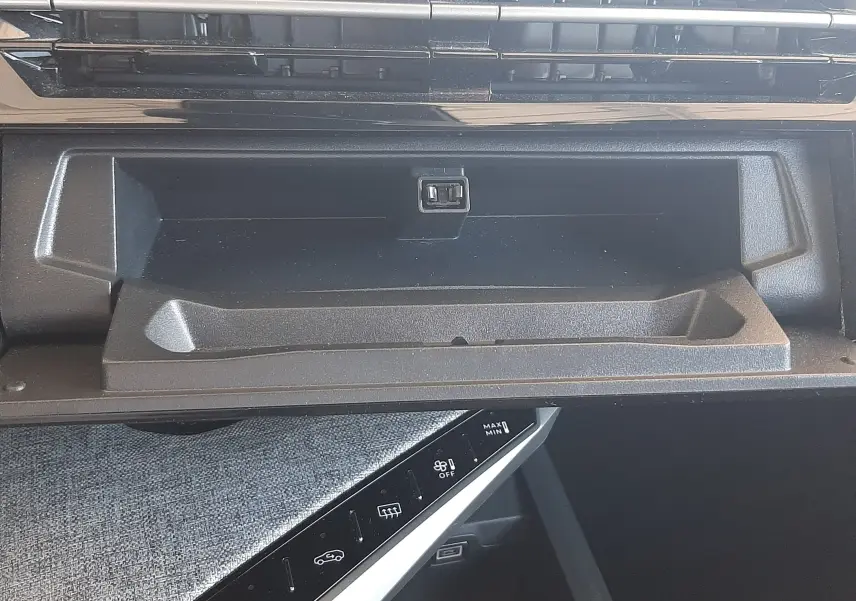 Gros plan intérieur sur la boîte à gants ouverte et la console centrale noire du Peugeot 5008 Hybrid blanc Okenite.