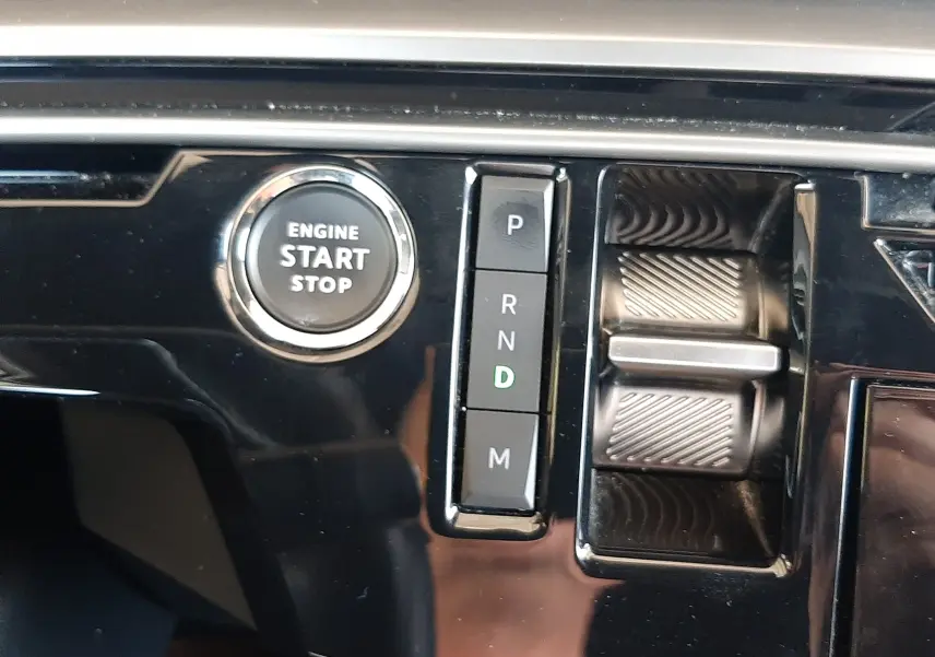 Détail de la console centrale du Peugeot 5008 Hybrid 2025 montrant le bouton start/stop et la sélection de boîte auto sur fond noir brillant.