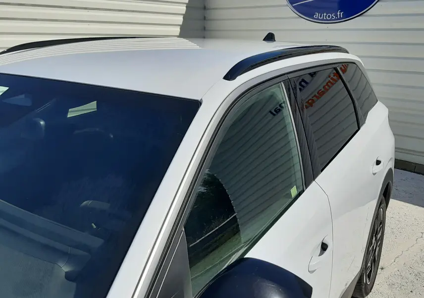 Vue 3/4 avant droit du Peugeot 5008 blanc Okenite, mettant en valeur le rétroviseur noir et les barres de toit noires.