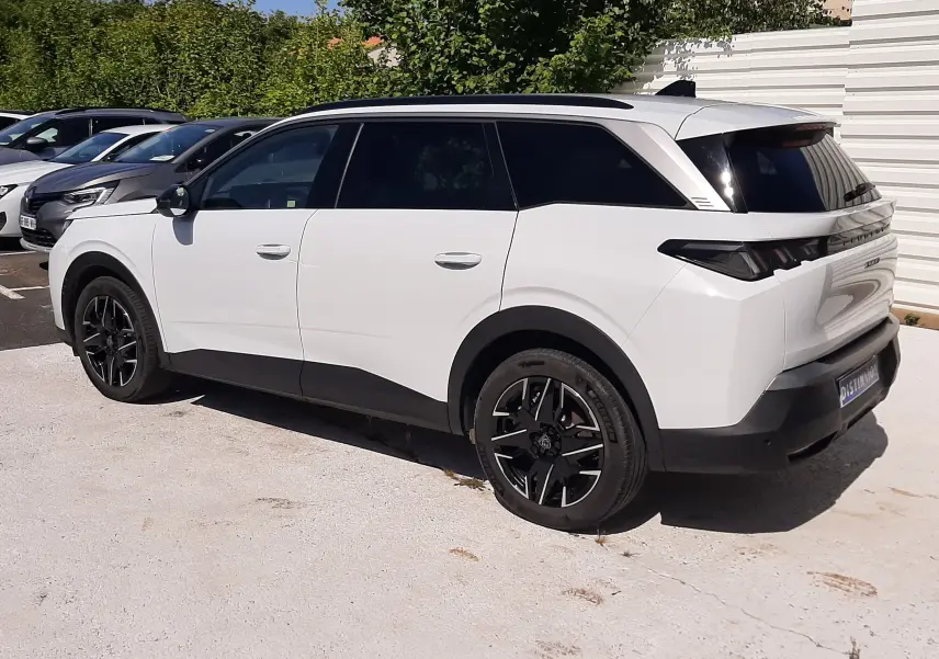 Vue 3/4 arrière droite d'un Peugeot 5008 blanc Okenite avec toit panoramique et jantes noires biton.