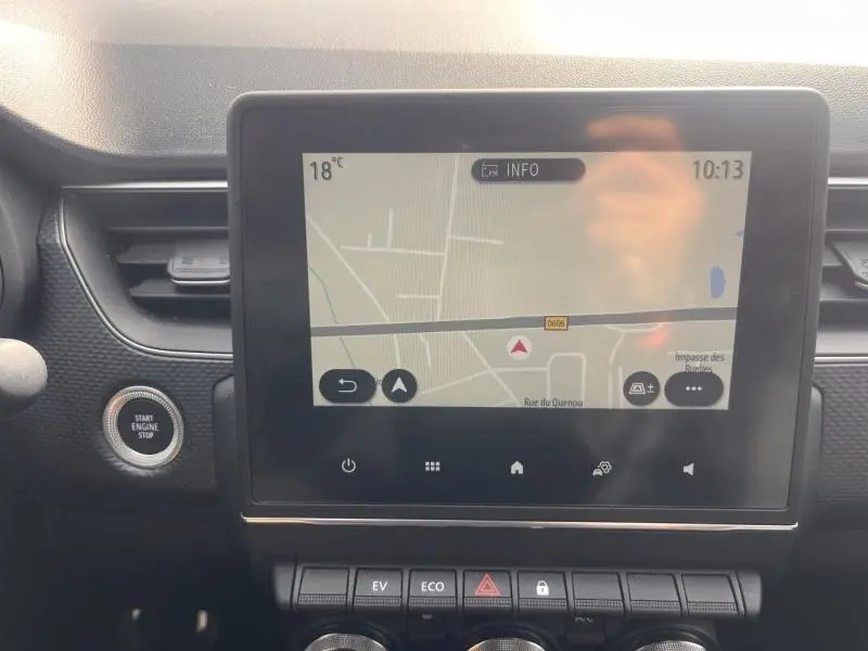 Vue intérieure centrée sur l'écran tactile du GPS du Renault Arkana blanc perle, avec bouton start engine stop visible à gauche.