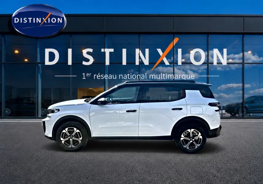 Vue de profil droit d'un Citroën C3 Aircross blanc avec toit noir, jantes alliage et vitres teintées, devant un showroom.