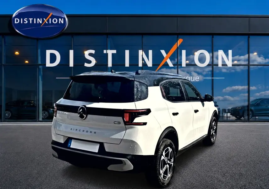 Vue 3/4 arrière droite d'un Citroën C3 Aircross blanc avec toit noir, garé devant une vitrine Distinxion.