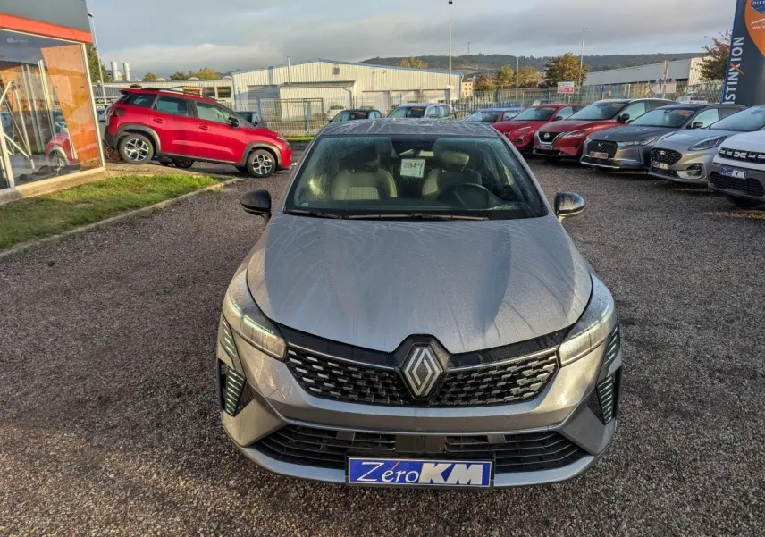 Renault Clio 2025 gris schiste vue de face, avec calandre noire et phares LED distinctifs, sur parking extérieur.
