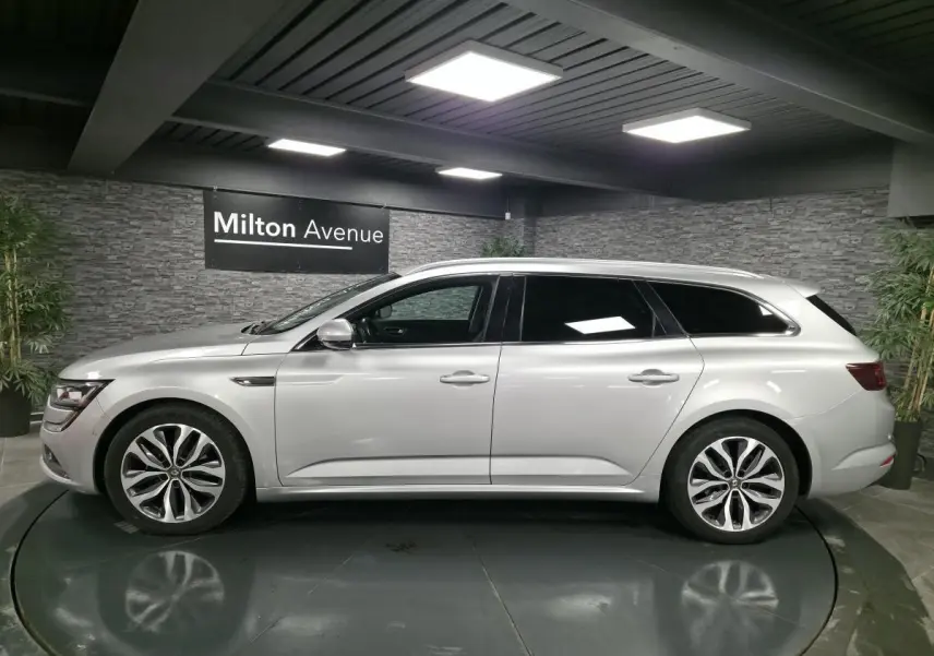 Profil côté gauche de la Renault Talisman Estate gris platine 2018 dans un showroom avec éclairage moderne.