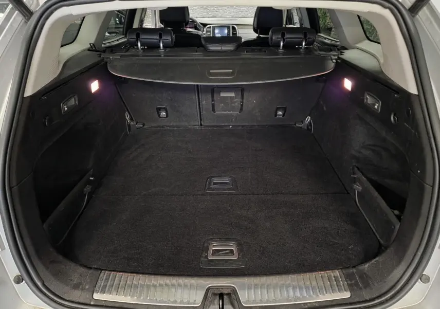 Coffre ouvert vu de l'arrière d'une Renault Talisman Estate gris, avec cache-bagages et éclairage intérieur allumé.