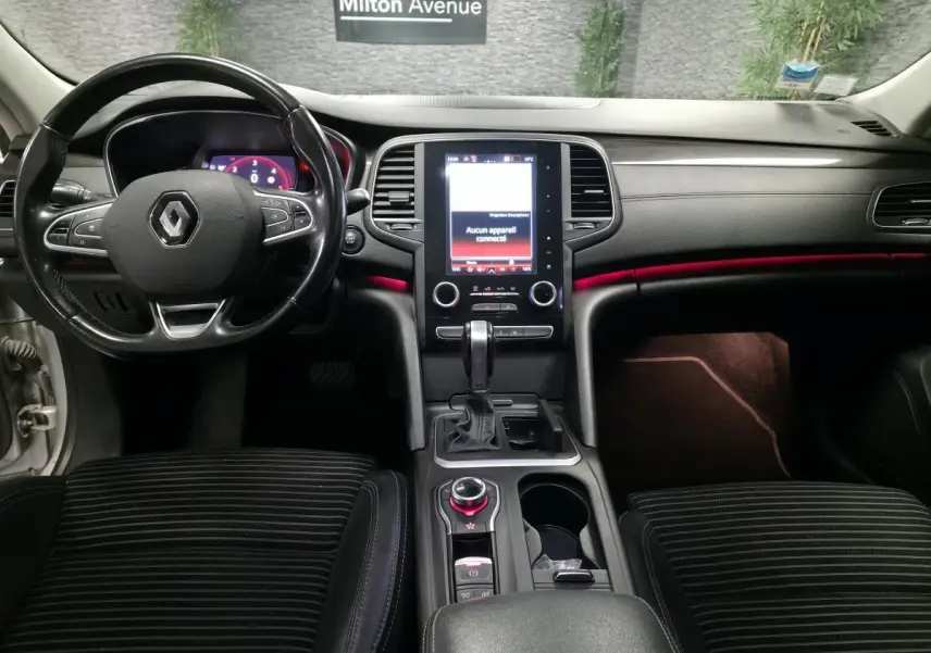 Intérieur avant d'une Renault Talisman Estate gris, tableau de bord noir avec éclairage d'ambiance rouge et écran tactile central.