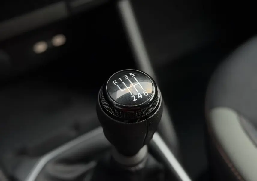 Gros plan sur le levier de vitesses manuel du Dacia Duster TCE 4x2 MHEV 130, intérieur sombre avec surpiqûres brun cuivré.