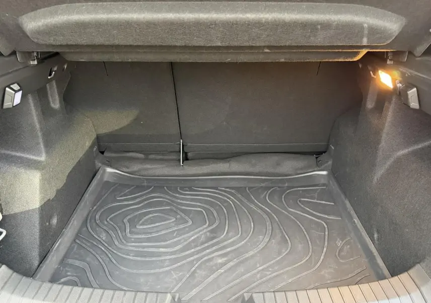 Coffre ouvert du Dacia Duster 2025 beige Sandstone, vue intérieure montrant le tapis de sol en caoutchouc et l'éclairage latéral.