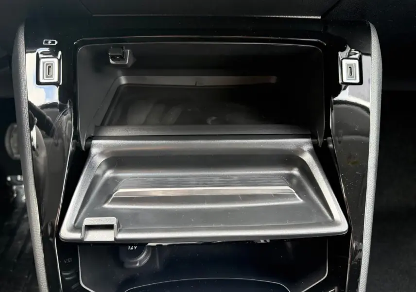Gros plan intérieur sur le rangement central ouvert de la Peugeot 208 Hybrid 145 gris avec prise USB et finition noire brillante.