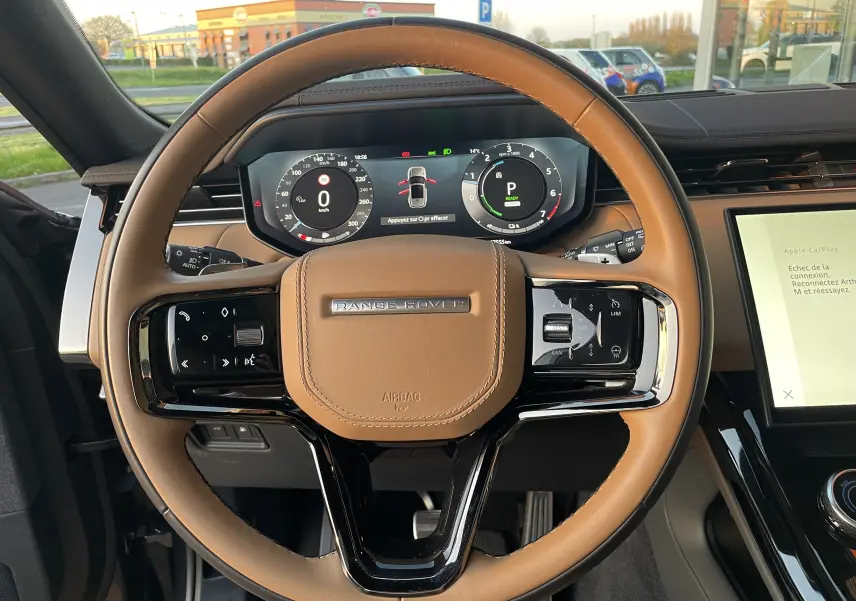 Vue rapprochée du volant en cuir marron du Range Rover Sport P440 HSE R-Dynamic 2023 avec tableau de bord numérique allumé.