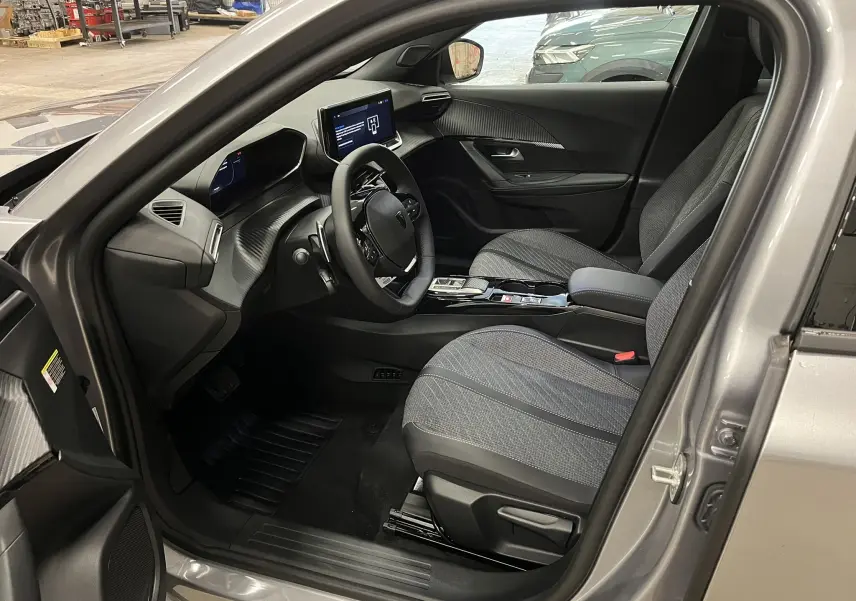 Vue intérieure côté conducteur du Peugeot 2008 gris Artense 2025, montrant sièges tissu et tableau de bord moderne.