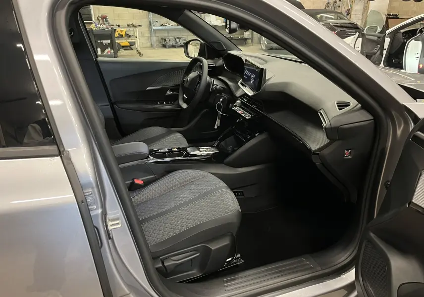 Vue intérieure côté conducteur du Peugeot 2008 gris Artense 2025, montrant le tableau de bord moderne et les sièges tissu gris.