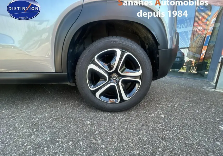 Gros plan sur la roue avant droite du Citroën C3 Aircross gris foncé avec jante 16 pouces bicolore et élargisseur noir mat.