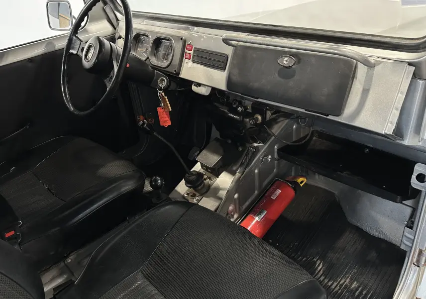 Intérieur du Suzuki Across LJ80 Cabriolet gris 1981 vu côté conducteur, avec tableau de bord simple et extincteur au sol.