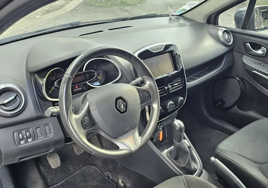 Intérieur côté conducteur de la Renault Clio IV grise, montrant le volant, tableau de bord et console centrale avec écran tactile.