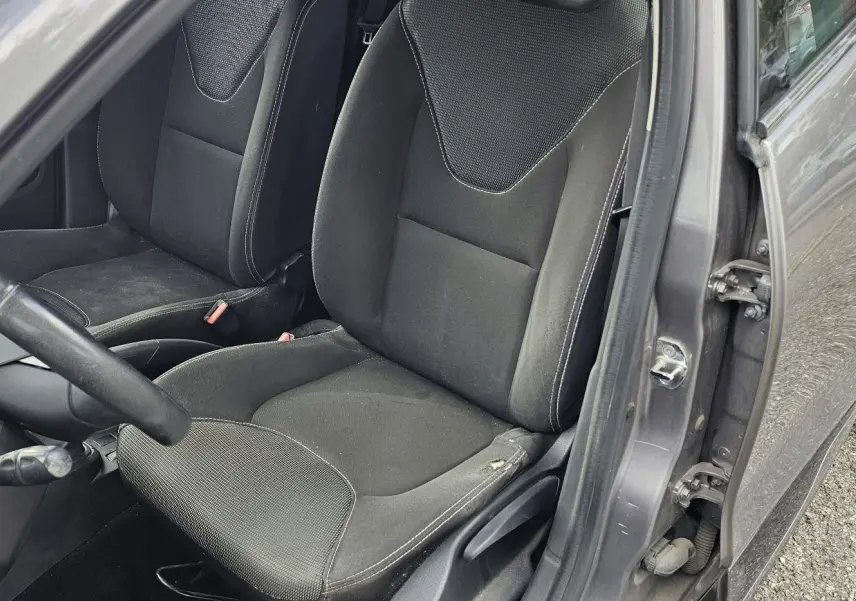 Vue intérieure côté conducteur de la Renault Clio IV grise de 2015, montrant les sièges en tissu noir et le volant.