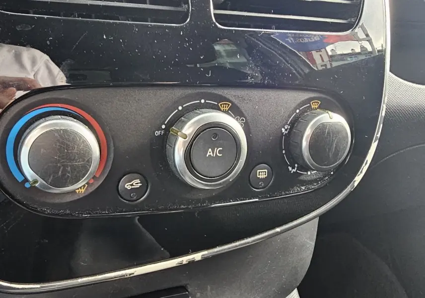 Commandes de climatisation avec réglages manuels et bouton A/C sur le tableau de bord noir d'une Renault Clio IV grise.