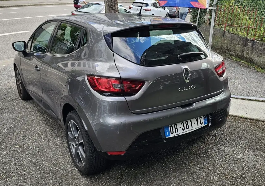 Renault Clio IV grise vue 3/4 arrière côté gauche, avec feux arrière rouges et plaque d'immatriculation française.