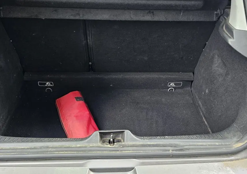 Coffre ouvert d’une Renault Clio IV grise de 2015, montrant un sac rouge à l’intérieur et la garniture noire du coffre.