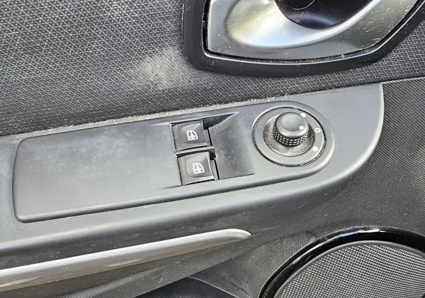 Gros plan sur la commande des vitres électriques et le réglage des rétroviseurs côté conducteur d'une Renault Clio IV grise.