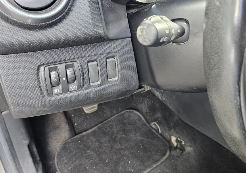 Vue rapprochée du tableau de bord côté gauche d'une Renault Clio IV grise, montrant les commandes d'éclairage et le volant.