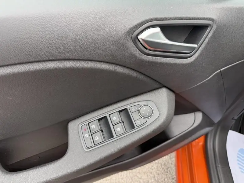 Gros plan sur la porte côté gauche d'une Renault Clio V orange 2025, montrant les commandes des vitres et la poignée intérieure.