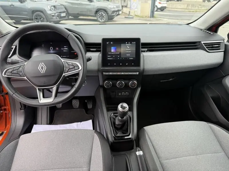 Vue intérieure avant de la Renault Clio V SCE 65 Evolution 2025 orange, tableau de bord moderne avec écran tactile et boîte manuelle.