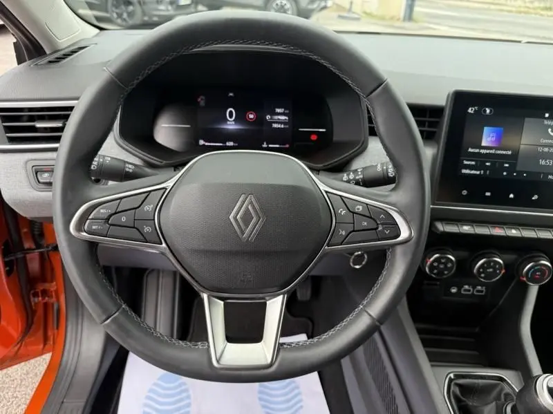 Vue rapprochée du volant noir de la Renault Clio V orange 2025, affichage numérique et console centrale visible.