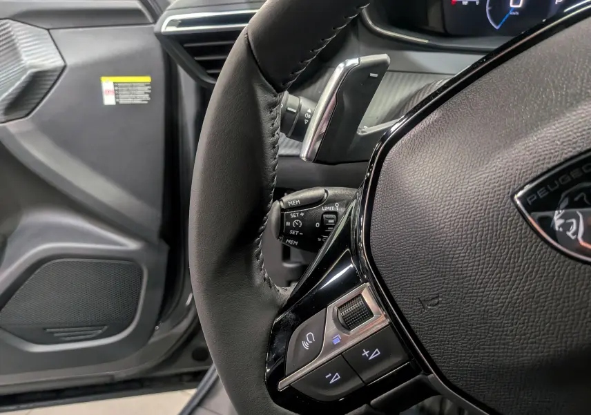 Gros plan sur le volant cuir noir du Peugeot 2008 Hybrid 145 e-DCS6 Allure avec commandes intégrées, intérieur gris.