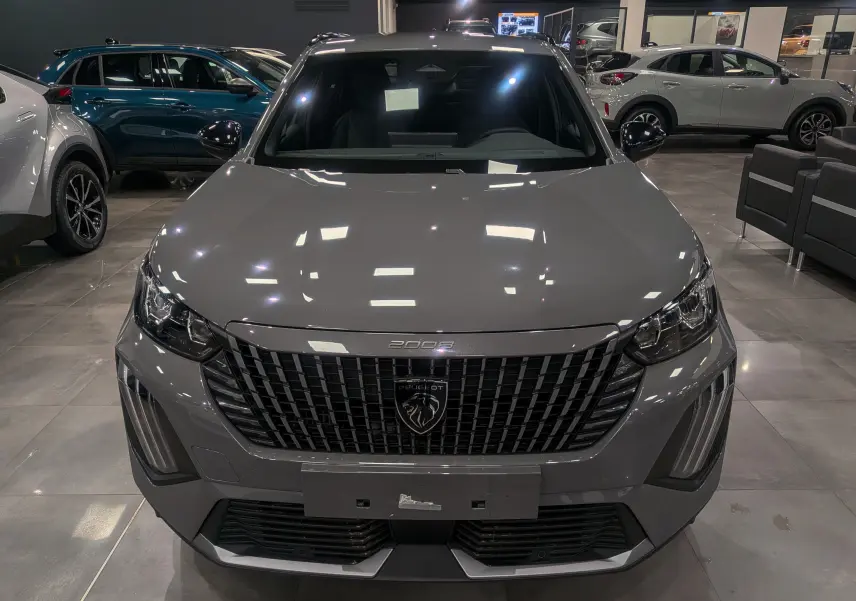 Vue frontale d'un Peugeot 2008 Hybrid 145 gris Sélénium avec calandre noire et éclairage LED en showroom.