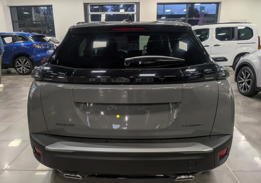 Vue arrière d'un Peugeot 2008 Hybrid 145 e-DCS6 Allure gris Sélénium dans un showroom lumineux.