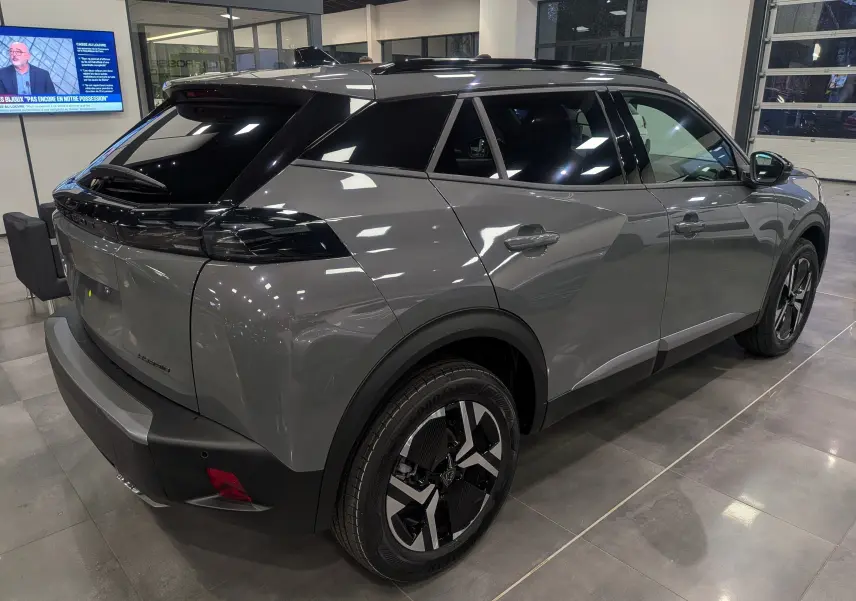 Vue 3/4 arrière droite d'un Peugeot 2008 Hybrid 145 gris Sélénium avec toit noir et jantes bicolores en showroom.