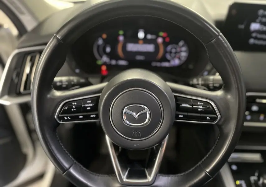 Gros plan sur le volant cuir noir du Mazda CX-60 2023 avec commandes intégrées et logo Mazda central.