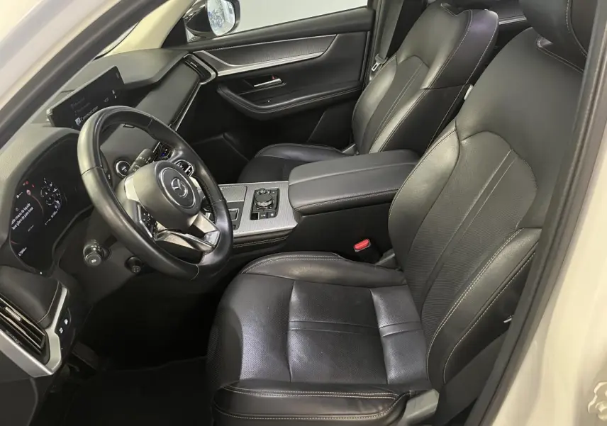 Intérieur du Mazda CX-60 blanc vu côté conducteur, sièges cuir noir avec surpiqûres bronze et tableau de bord moderne.