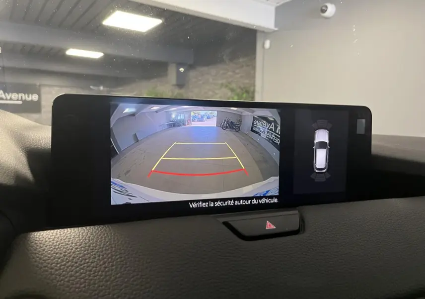 Écran central affichant la caméra de recul et la vue 360° du Mazda CX-60 blanc en stationnement intérieur.