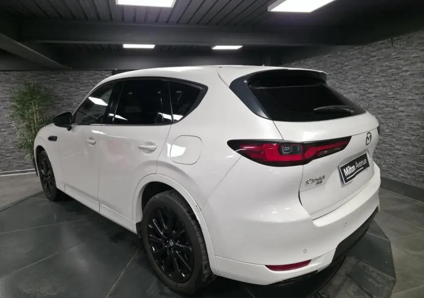 Vue 3/4 arrière droite du Mazda CX-60 blanc Arctic White avec jantes alliage noires et feux arrière LED dans un showroom.