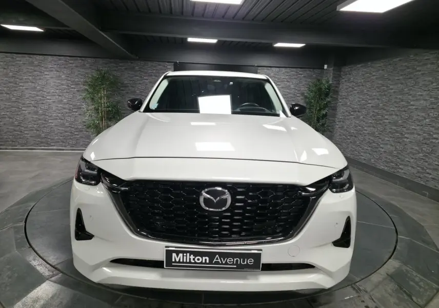 Vue frontale d'un Mazda CX-60 blanc avec calandre noire brillante et phares LED dans un showroom.