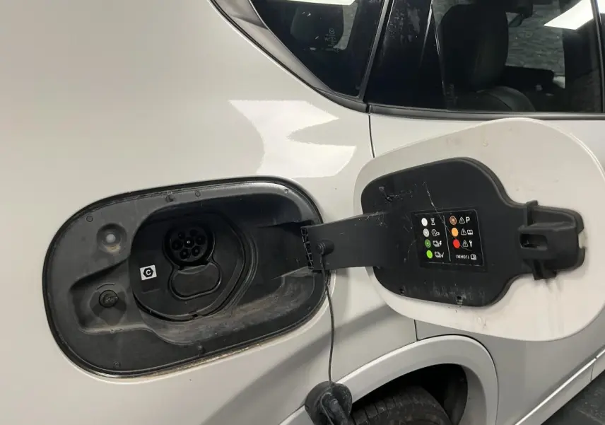 Prise de recharge ouverte côté gauche sur un Mazda CX-60 blanc hybride rechargeable, détail de la trappe et connecteur.