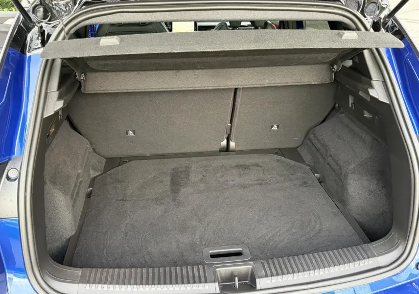 Coffre ouvert vu de l'arrière d'un Renault Austral bleu Iron avec intérieur de coffre noir et cache-bagages relevé.