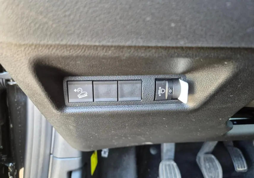 Gros plan sur les commandes de régulateur de vitesse et réglage des phares sous le tableau de bord côté conducteur du Jeep Avenger noir.