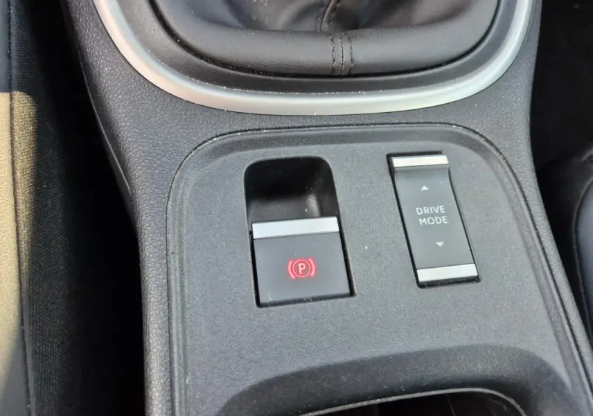 Gros plan sur la console centrale noire du Jeep Avenger 2024 montrant le frein à main électrique et le bouton Drive Mode.