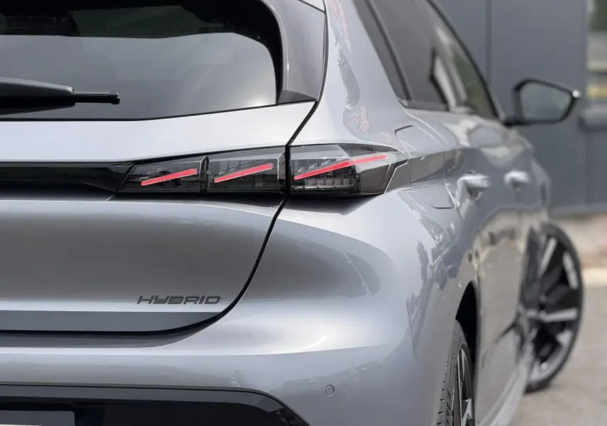Vue 3/4 arrière droite d'une Peugeot 308 Hybrid gris Artense avec feux arrière LED à trois griffes et jantes bi-ton.